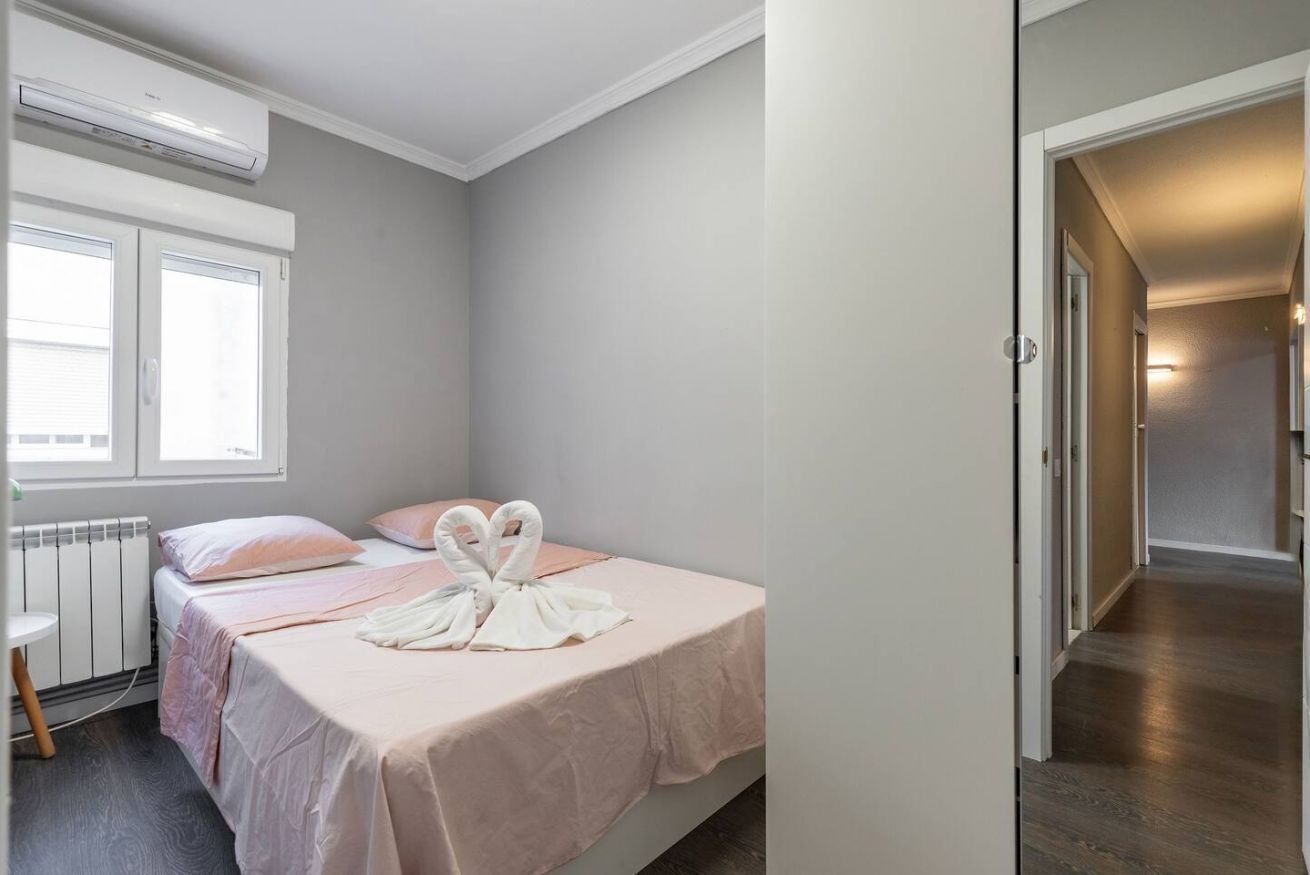 A bedroom with a bed, pillows, a radiator, an air conditioner, and a view of a hallway.