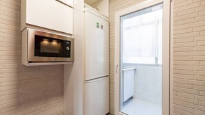 Une cuisine compacte équipée d’un four à micro-ondes, d’un réfrigérateur et d’une porte-fenêtre coulissante donnant sur un balcon.