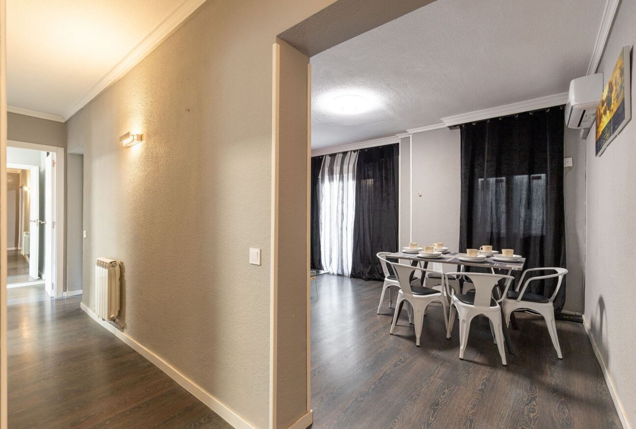 A hallway with a radiator, a dining area with a table and chairs, and a window with curtains.