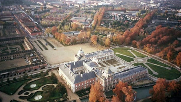 Vue aérienne d’un vaste ensemble de bâtiments historiques, doté de jardins symétriques et d’une cour centrale.