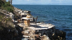 A stone bench by the sea with a bottle and bread, overlooking the water. - Exclusive Seafront Villa up to 18 – Breathtaking Views & Personal Chef & Daily maid Included! (Sparto)