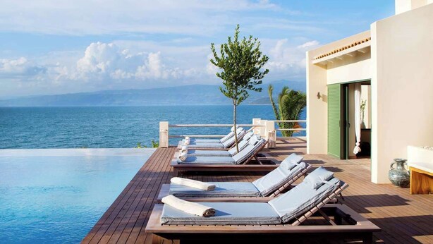 A wooden deck with lounge chairs and a small tree, overlooking a clear blue sea. - Exclusive Seafront Villa up to 18 – Breathtaking Views & Personal Chef & Daily maid Included! (Sparto)