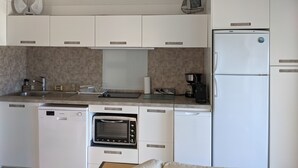 Cocina compacta con armarios blancos, horno empotrado, refrigerador y cafetera.