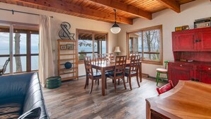 Een eethoek met een houten tafel en stoelen, een rode kast en grote ramen met uitzicht op een prachtig landschap.