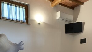 Een hotelkamer met een bed, een houten tafel met kop en schotel, een aan de muur bevestigde televisie en een raam met gordijnen.