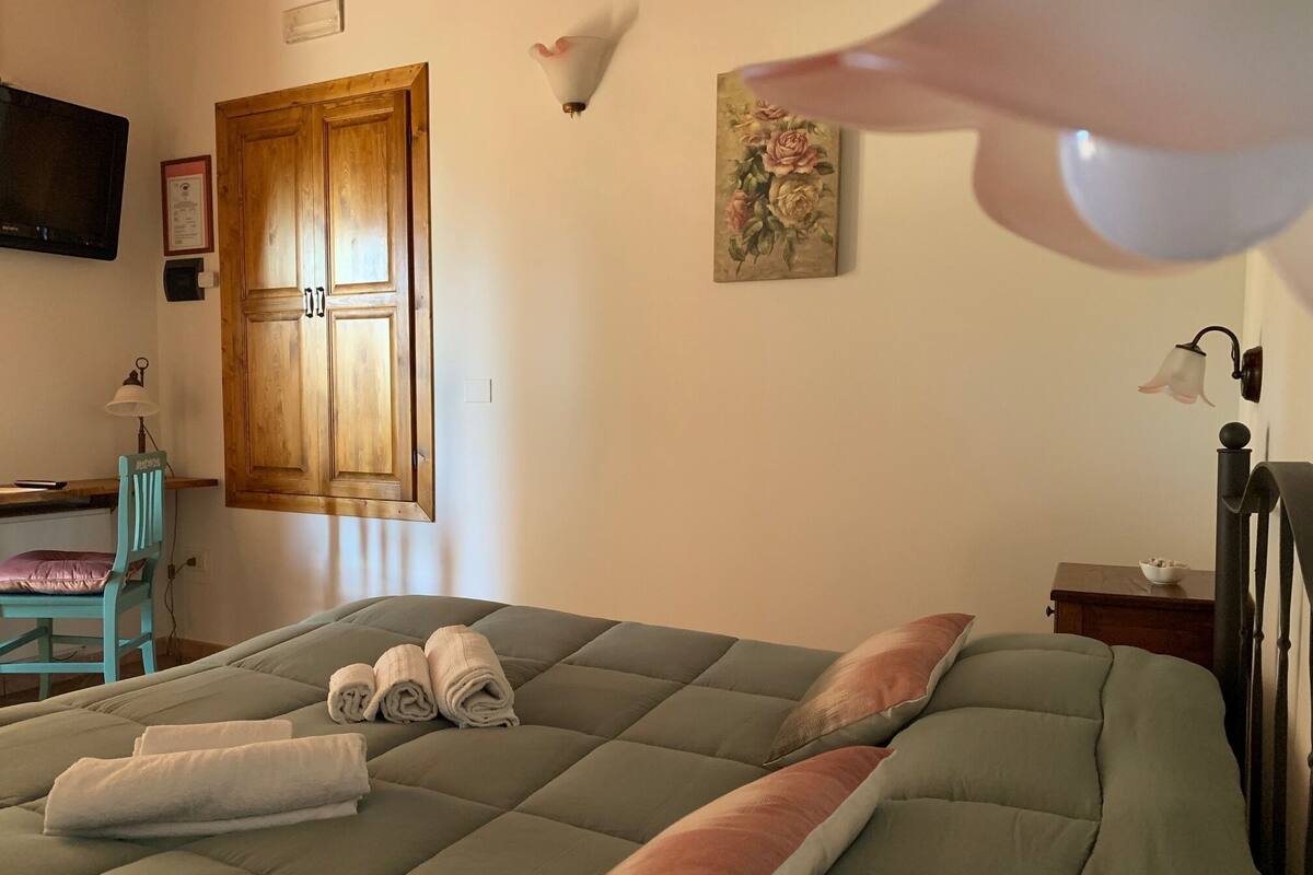 Een slaapkamer met een bed, een bureau, een stoel en een schilderij aan de muur.