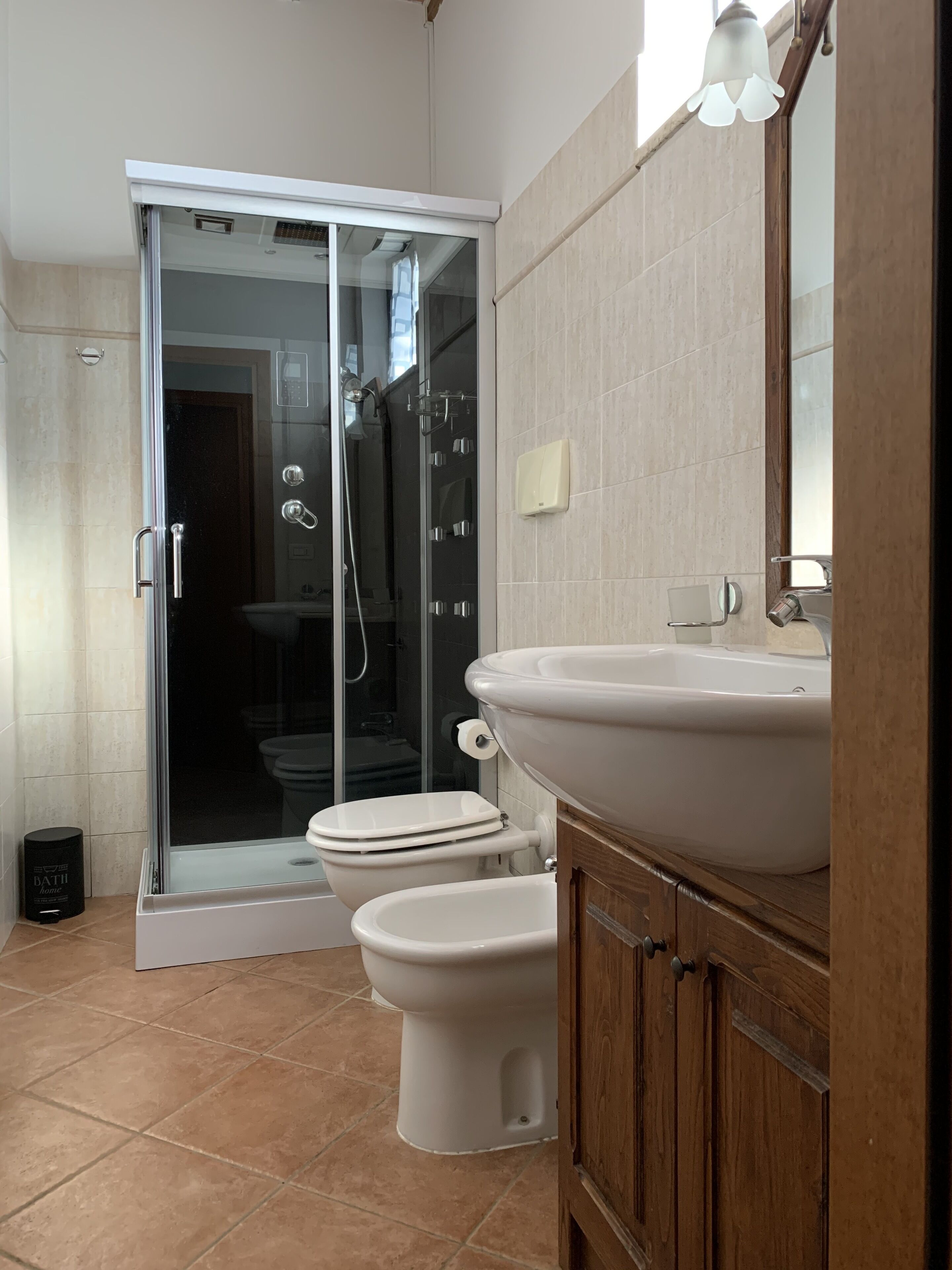 Un baño moderno con cabina de ducha de vidrio, inodoro blanco y tocador de madera con un lavamanos grande.