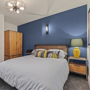 Une chambre à coucher comprenant un lit, une armoire en bois, une table de chevet, une lampe et un luminaire au plafond.