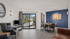 A modern living room with a TV, seating, and a dining area with a view through glass doors. - No1 Highpoint -Luxury 2 bed Sea view Apartment with onsite indoor swimming pool (Saundersfoot)