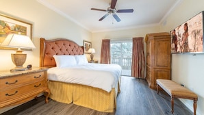 Een stijlvol ingerichte slaapkamer met een groot bed, een houten dressoir, een bankje en een plafondventilator.