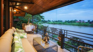 A wooden deck with a sofa, table, and chairs overlooking a river. - Cattani's Riverside Home (Ayutthaya)