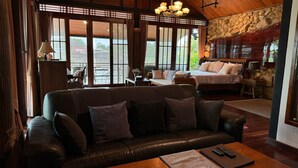 A cozy living room with a leather sofa, a bed with pillows, and a stone wall. - Cattani's Riverside Home (Ayutthaya)