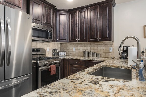 A kitchen with dark wood cabinets, stainless steel appliances, a granite countertop, and a built-in sink.