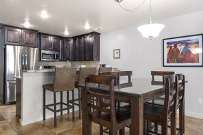 Une cuisine moderne avec des meubles en bois foncé, des appareils électroménagers en acier inoxydable et un coin repas comprenant des chaises en bois et une table en verre.