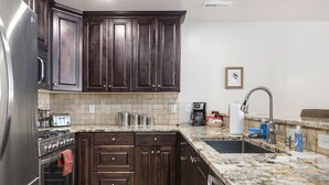 A kitchen with dark wooden cabinets, a stainless steel refrigerator, a granite countertop, a sink, and a tiled backsplash. - Close to Town & National Parks | Pool & Hot Tub (Moab)