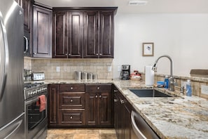 A kitchen with dark wooden cabinets, a stainless steel refrigerator, a granite countertop, a sink, and a tiled backsplash. - Close to Town & National Parks | Pool & Hot Tub (Moab)