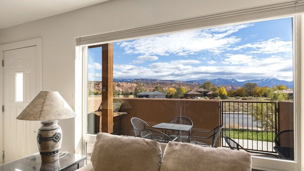 A balcony with a view of mountains and a lake, furnished with a table and chairs. - Close to Town & National Parks | Pool & Hot Tub (Moab)