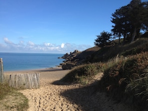 A beach with a wooden fence, sandy terrain, and a rocky cliff.