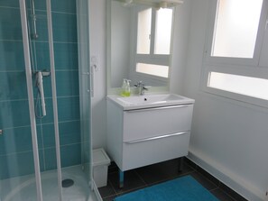 Un baño con ducha de vidrio, un lavamanos blanco con un espejo arriba y una alfombra de baño azul en el suelo.