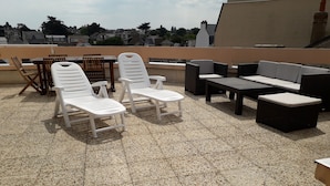 Terraço no telhado com cadeiras de lounge brancas, uma mesa e um sofá.
