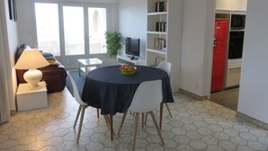 Uma sala de jantar com uma mesa posta para dois, uma televisão, uma estante de livros e uma geladeira vermelha.