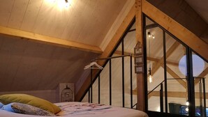 Un dormitorio con techo inclinado, una cama con colcha estampada, una lámpara colgante y vistas por una ventana.