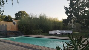 Una piscina con cubierta de madera, rodeada de follaje y una valla de madera.