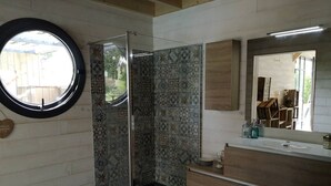 Un baño con cabina de ducha de vidrio, un ventanal redondo y salpicadero de azulejos.