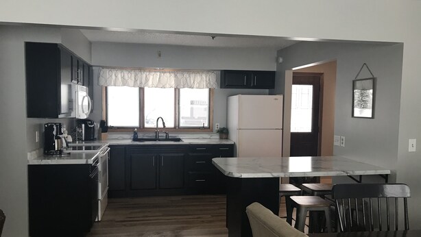 A modern kitchen with dark cabinets, a white refrigerator, and a marble countertop. - Oak & Arrow Cabin On Bluedog Lake, Waubay - Hunting, Fishing, Vacation (Waubay)