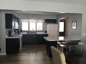 A modern kitchen with dark cabinets, a white refrigerator, and a marble countertop.