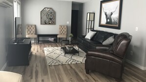 A living room with a dark brown leather sofa, two armchairs, a coffee table, and a rug. There is a large mirror on the wall and a framed picture above the sofa. - Oak & Arrow Cabin On Bluedog Lake, Waubay - Hunting, Fishing, Vacation (Waubay)