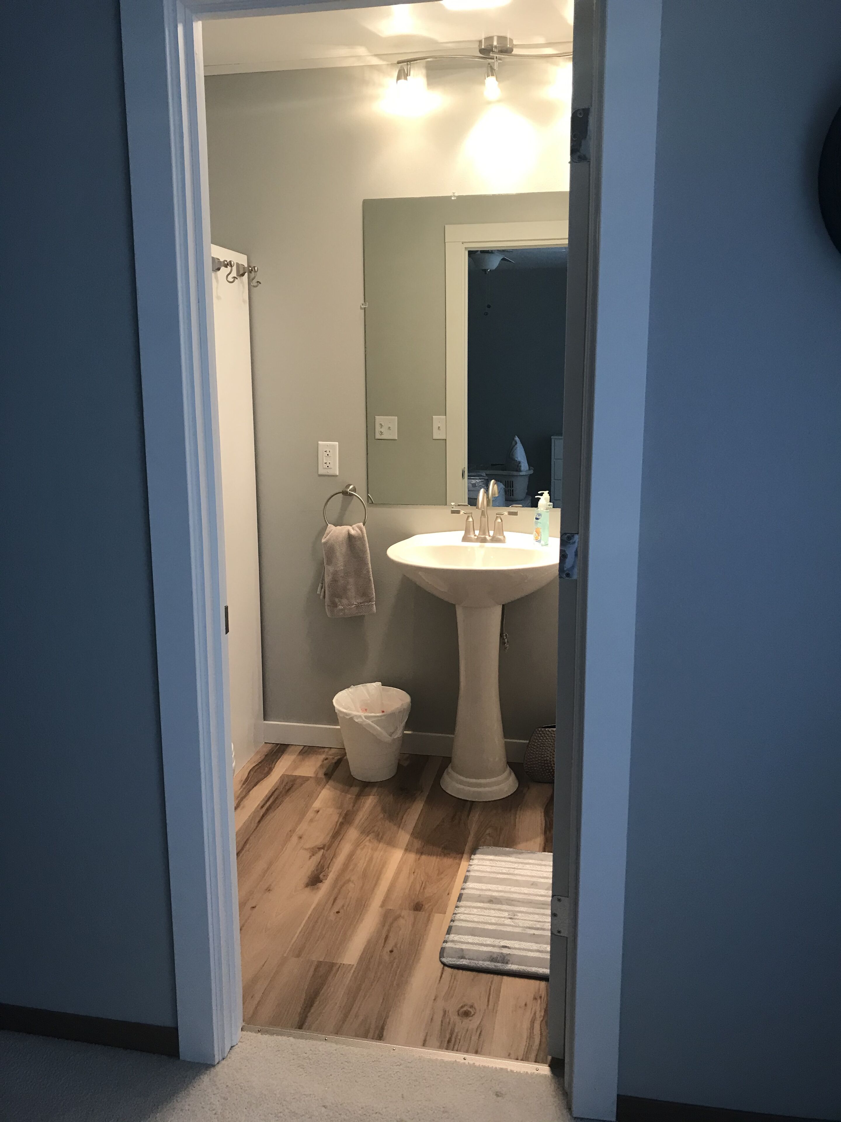 Une salle de bain avec un lavabo sur colonne, un porte-serviettes, une poubelle et un plancher en bois.