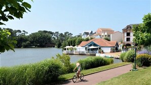 Un sendero junto al lago con un ciclista, un barco amarrado y edificios con tejados rojos.