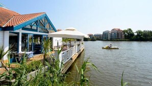 Un restaurante a la orilla del río con terraza y un bote en el agua.