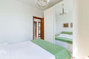 Une chambre à coucher avec un lit, une couvre-lit à motifs verts, un lustre et une porte donnant sur une autre pièce.