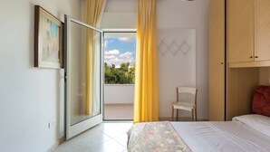 Ein Schlafzimmer mit Bett, Stuhl, Kleiderschrank und einer Schiebetür zu einem Balkon.