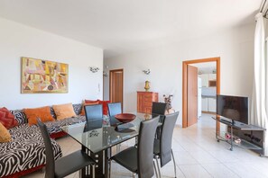 Un salon moderne avec une table à manger en verre, des chaises noires, un canapé à motifs zébrés et un téléviseur posé sur un meuble.