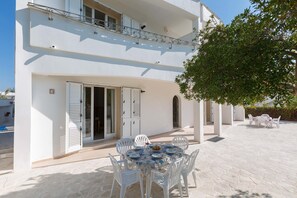 Un bâtiment à deux étages doté d’un balcon, d’une terrasse avec une table et des chaises, et d’un arbre qui offre de l’ombre.