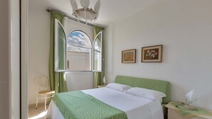 Ein Schlafzimmer mit einem Bett, einem Sessel, einem Nachttisch und einem Fenster mit Vorhängen.