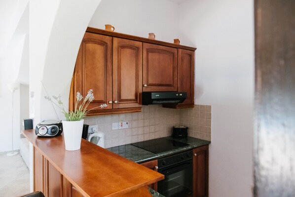 A modern kitchen with wooden cabinets, a black stove, and a white countertop. - Aphrodite - 3 Bedroom Villa with Swimming Pool (Neo Chorio)