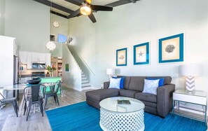 Ein modernes Wohnzimmer mit einer Couch, einem Couchtisch und einem Essbereich. Eine Treppe führt zu einer oberen Ebene.