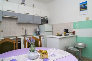 A modern kitchen with white cabinets, a microwave, a coffee maker, and a sink. There is a dining table with a purple tablecloth and a vase of flowers.