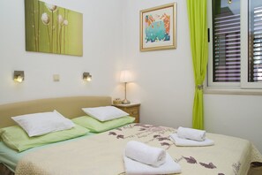 A hotel room with a bed, pillows, a nightstand with a lamp, a framed picture on the wall, and a window with curtains.