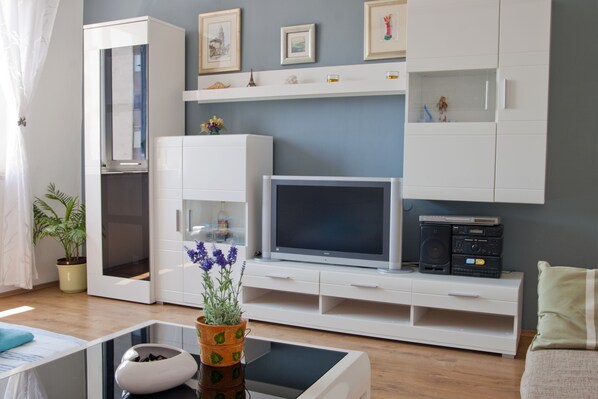 A modern living room with a flat-screen TV, white cabinets, a potted plant, and a coffee table.