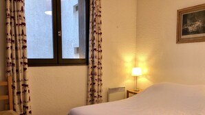 A bedroom with a large bed, a nightstand with a lamp, and curtains with a pattern.