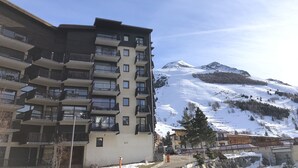 A multi-story building with balconies, a ski slope in the background, and a mountainous landscape.