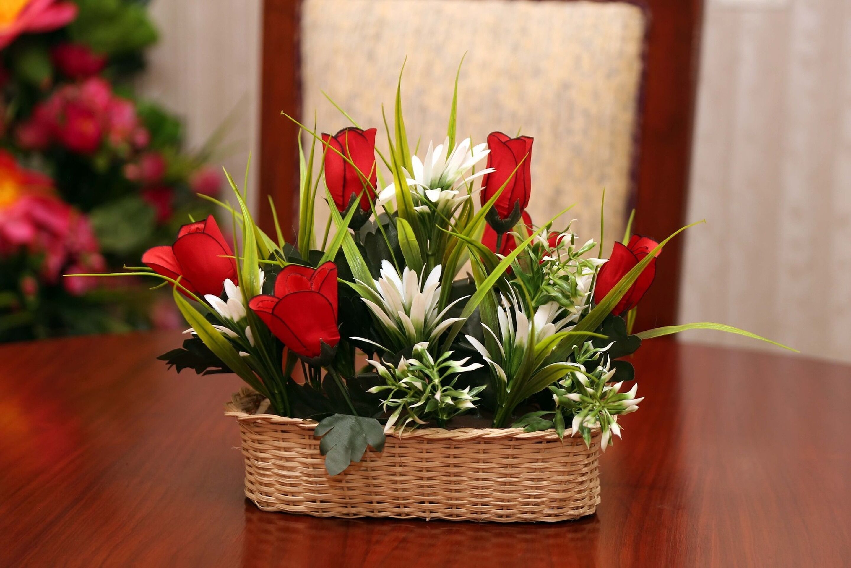 A wicker basket filled with red and white flowers placed on a wooden table.