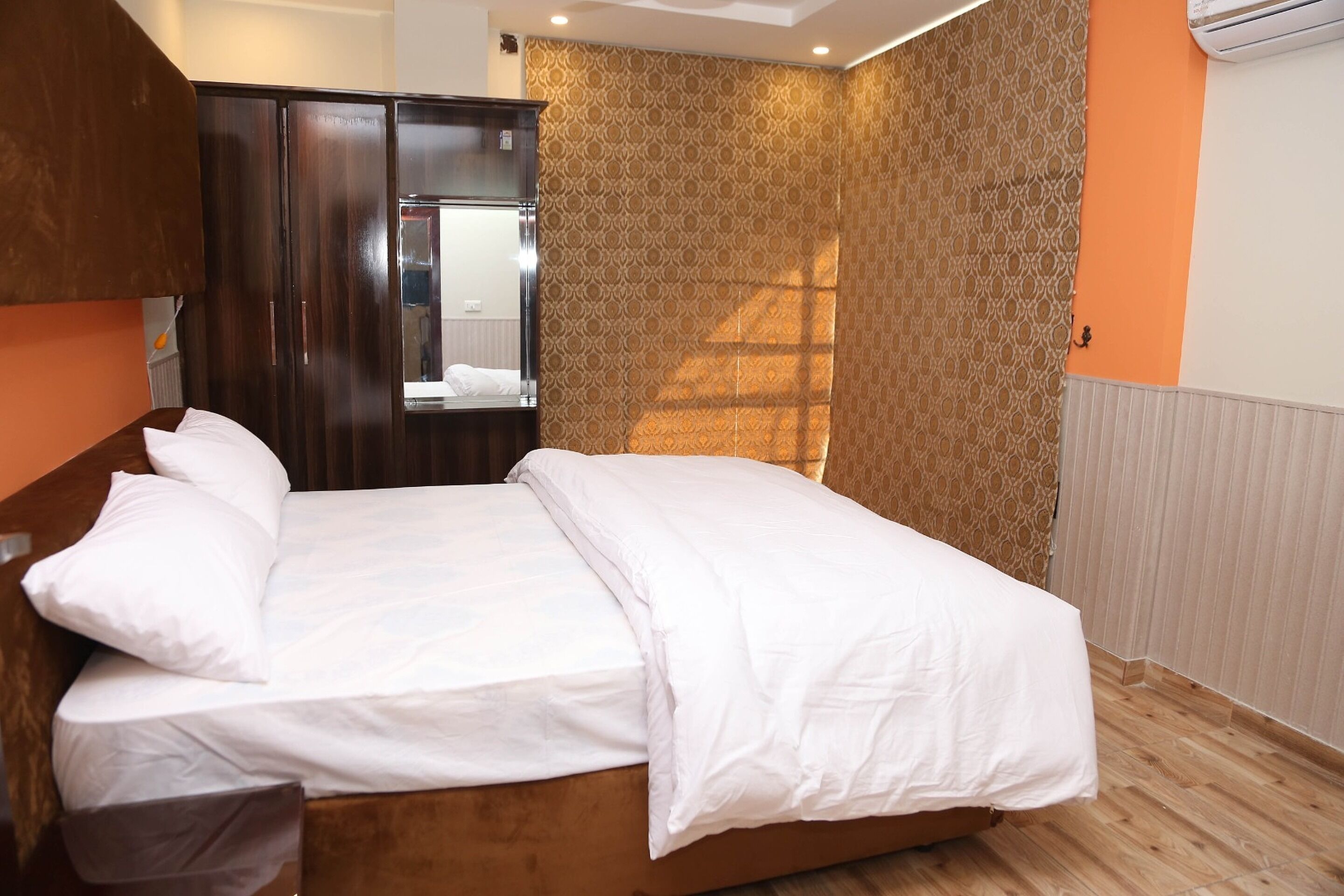 Una cama bien tendida en una habitación con un armario de madera, papel tapiz estampado y un radiador.