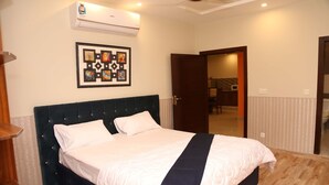 A bedroom with a bed, a wall-mounted air conditioner, and a framed artwork. - Hak Mall Suites (Rawalpindi)