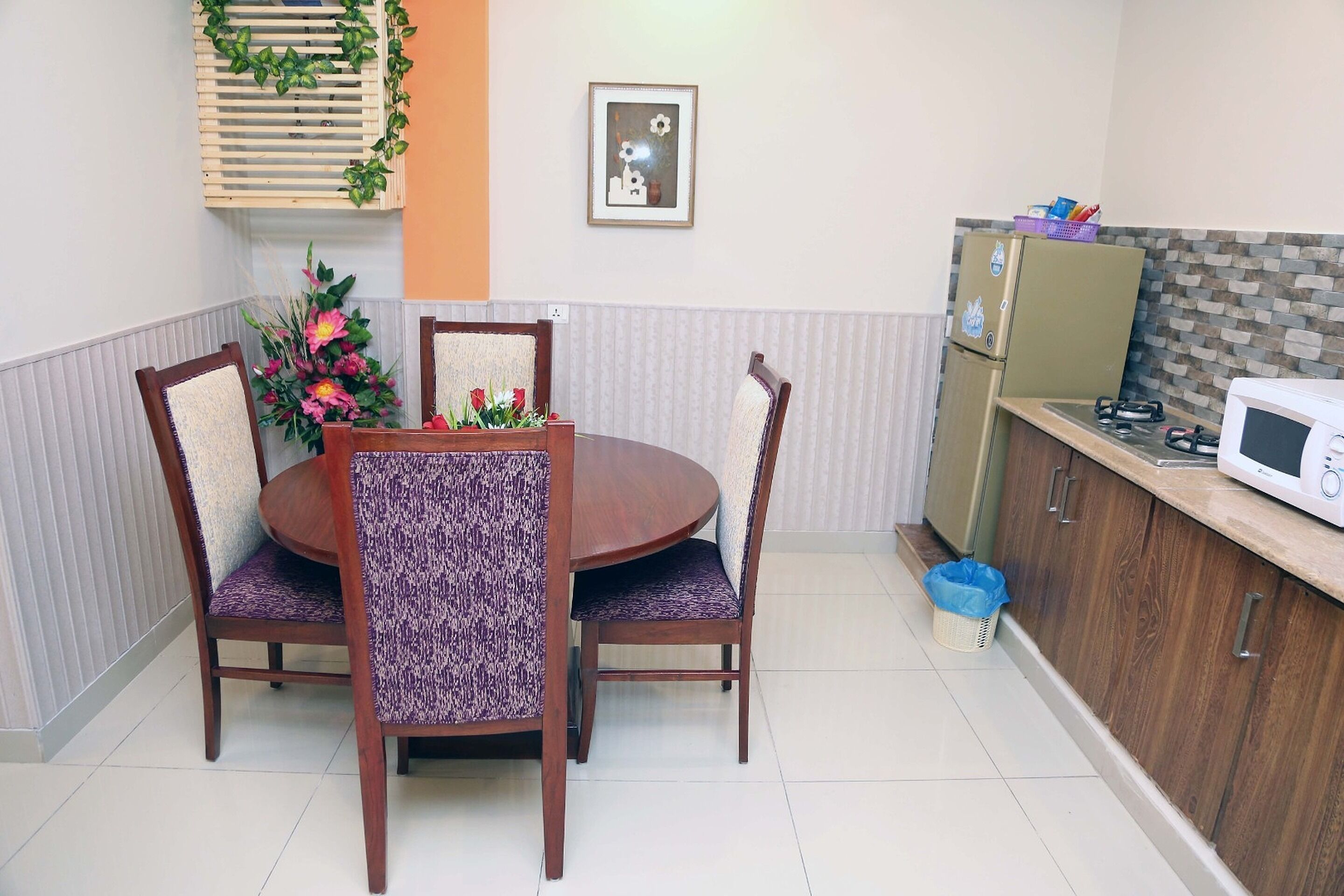 A dining area with a round table and four chairs, a refrigerator, and a microwave on the adjacent counter.